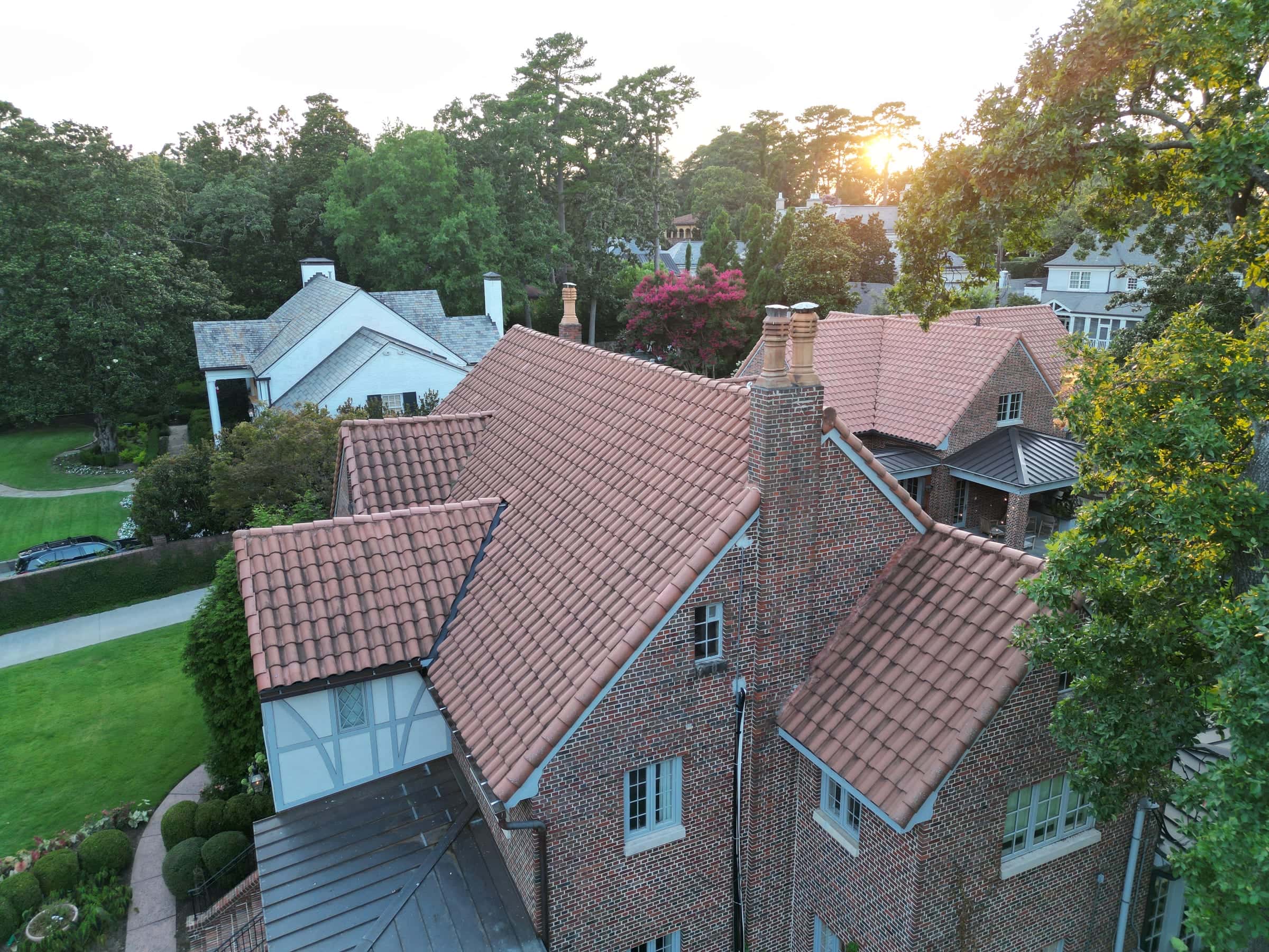 Red clay tile roof on a brick Tudor home at sunset, aerial view