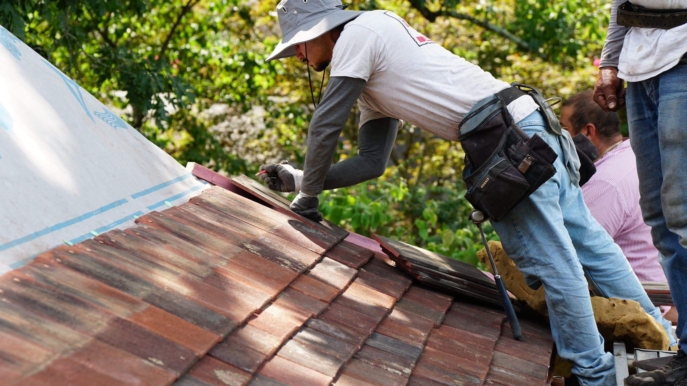 Cougill Roofing crew relaying salvaged clay tiles over new underlayment on a historic home