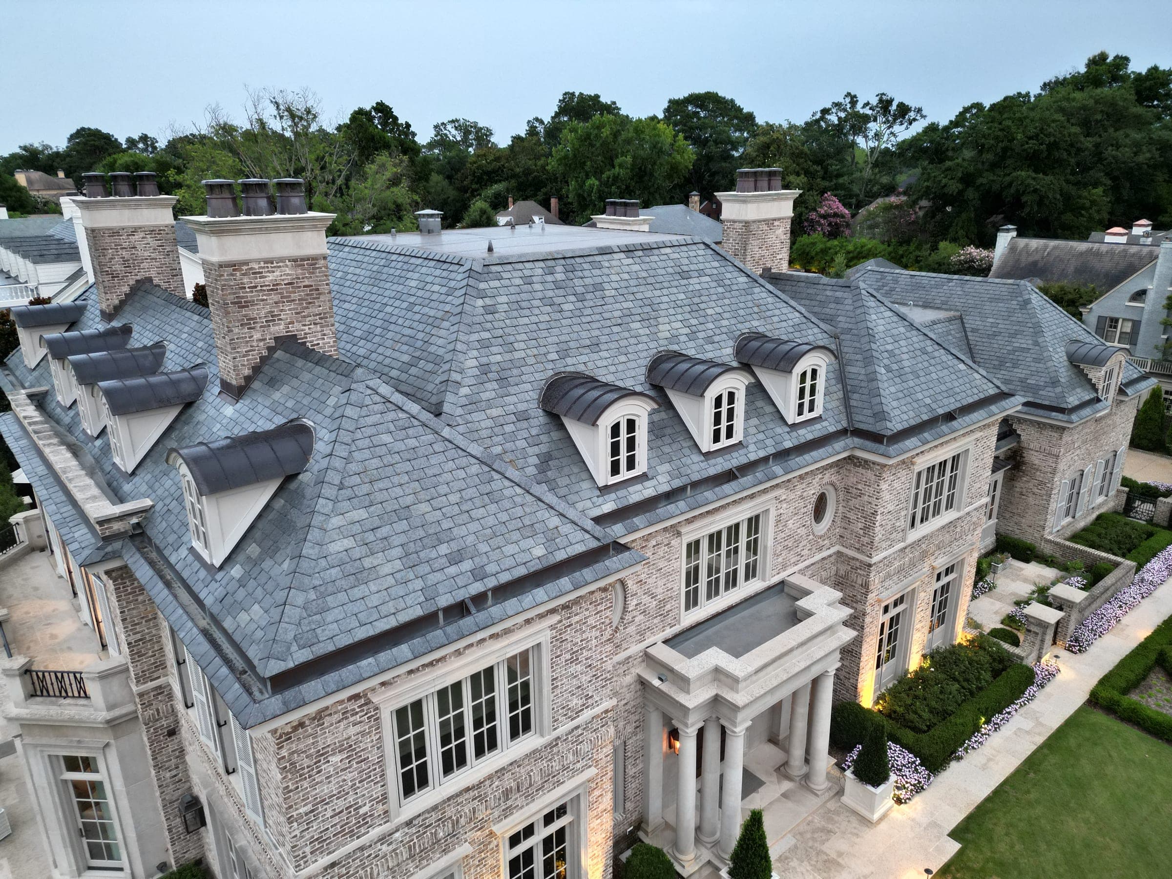 Aerial view of a large stone estate with a gray natural slate roof and multiple chimneys, installed by Cougill Roofing