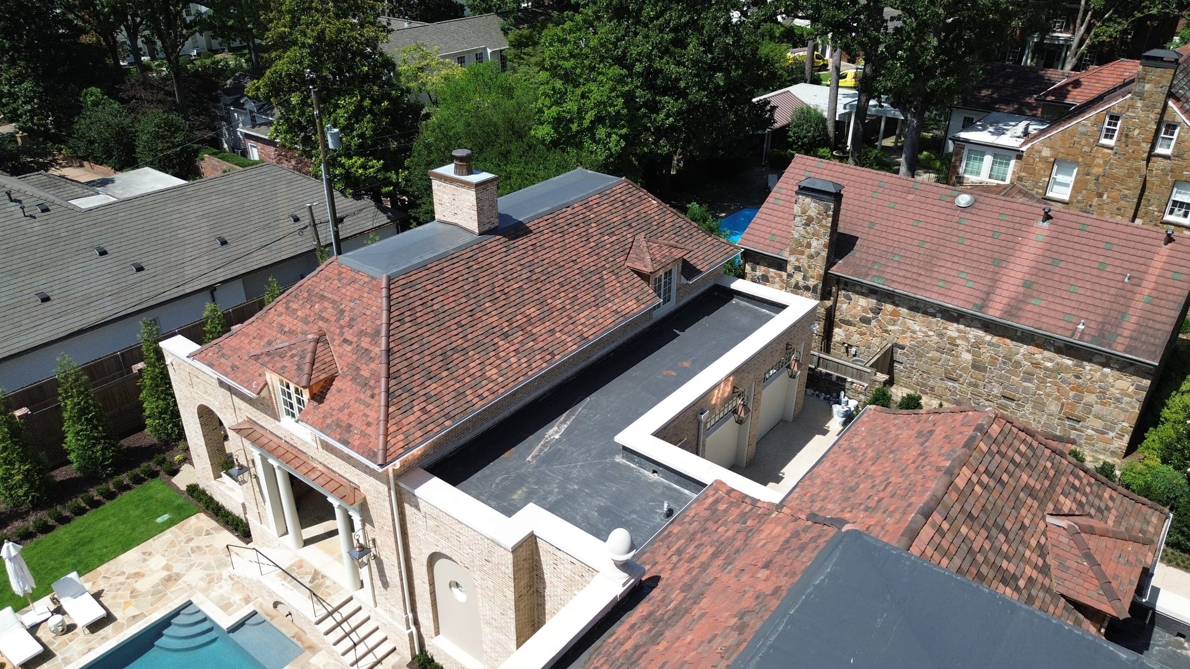 Aerial view of low-slope membrane roof sections between clay tile roof planes on a large property