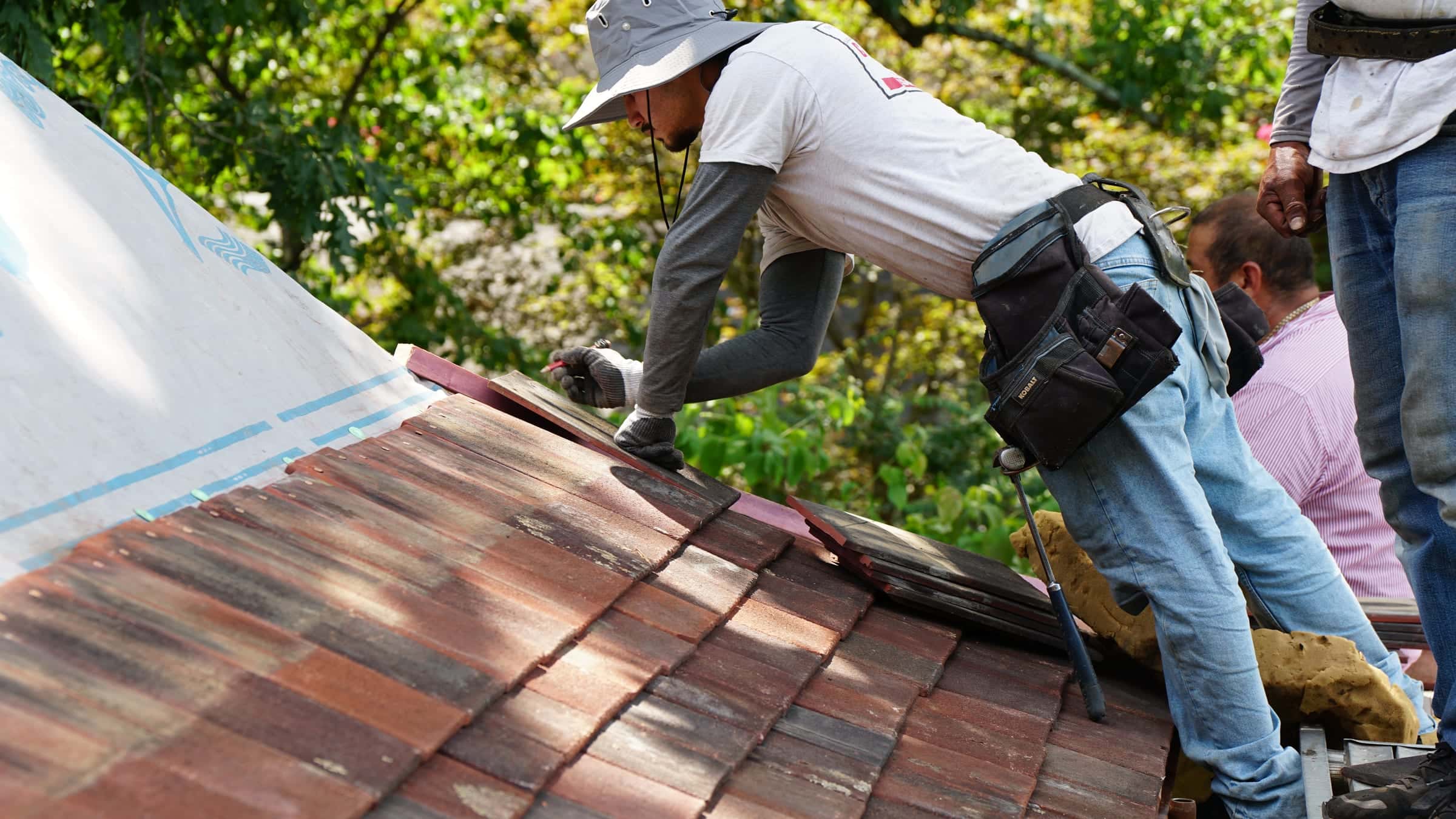 Cougill Roofing crew relaying salvaged clay tiles over new underlayment on a historic home