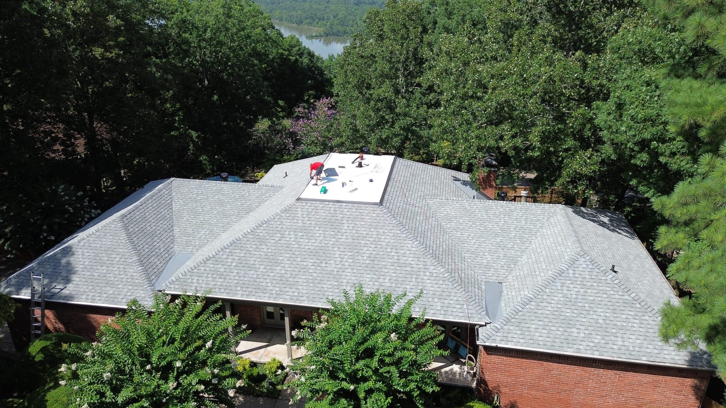 Cougill Roofing crew replacing a roof on a brick home surrounded by trees