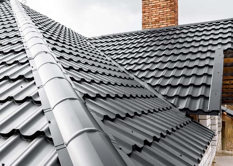 Dark metal roof panels with a ridge cap and brick chimney